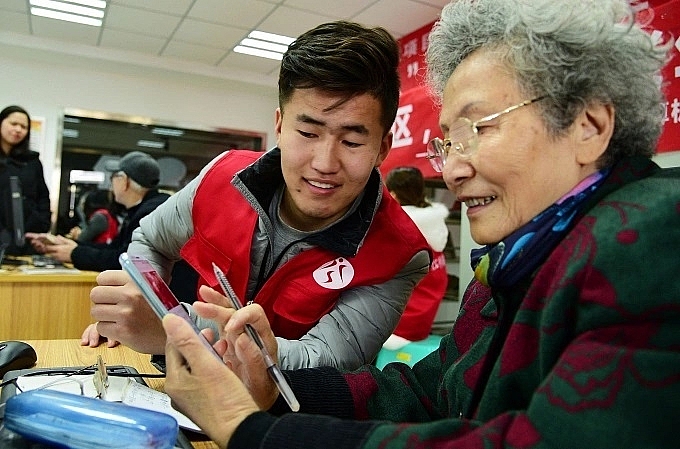Một tình nguyện viên hướng dẫn một phụ nữ cao tuổi cách sử dụng smartphone ở tỉnh Giang Tô. Ảnh:AFP Một tình nguyện viên hướng dẫn một phụ nữ cao tuổi cách sử dụng smartphone ở tỉnh Giang Tô. Ảnh:AFP