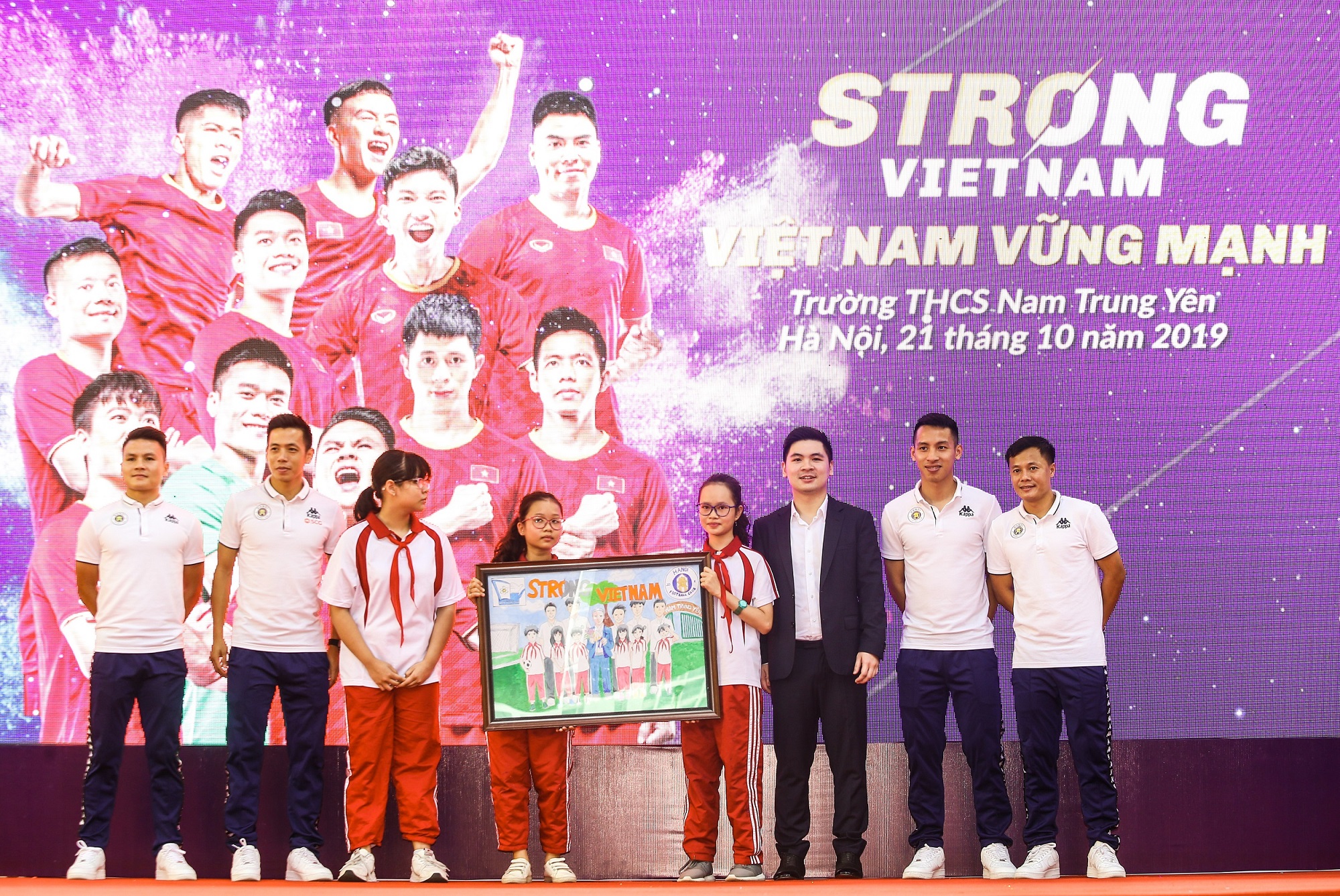 C&aacute;c cầu thủ CLB b&oacute;ng đ&aacute; H&agrave; Nội v&agrave; Trưởng Ban tổ chức chương tr&igrave;nh &ldquo;Strong Vietnam&rdquo; Đỗ Vinh Quang nhận qu&agrave; l&agrave; bức tranh từ c&aacute;c em học sinh THCS Nam Trung Y&ecirc;n