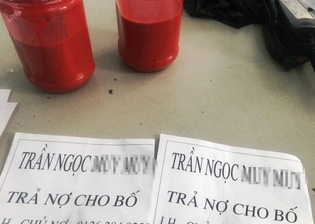 Lực lượng C&ocirc;ng an ph&aacute;t hiện c&aacute;c đối tượng mang theo một số vật dụng gồm 2 b&igrave;nh sơn m&agrave;u đỏ v&agrave; c&aacute;c tờ giấy A4, in d&ograve;ng chữ &ldquo;Trần Ngọc M. M. &ndash; trả nợ cho bố&hellip;&rdquo;. Ảnh: D&acirc;n tr&iacute;